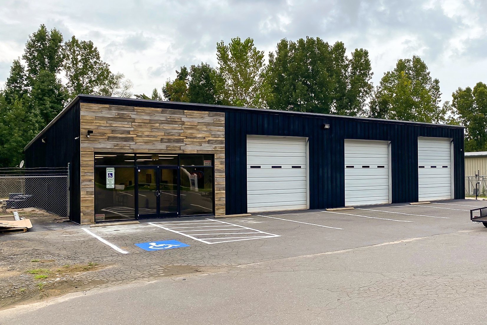 Metal building storefront with URESTONE reclaimed faux wood panels, black ribbed siding, and three white roll-up doors.