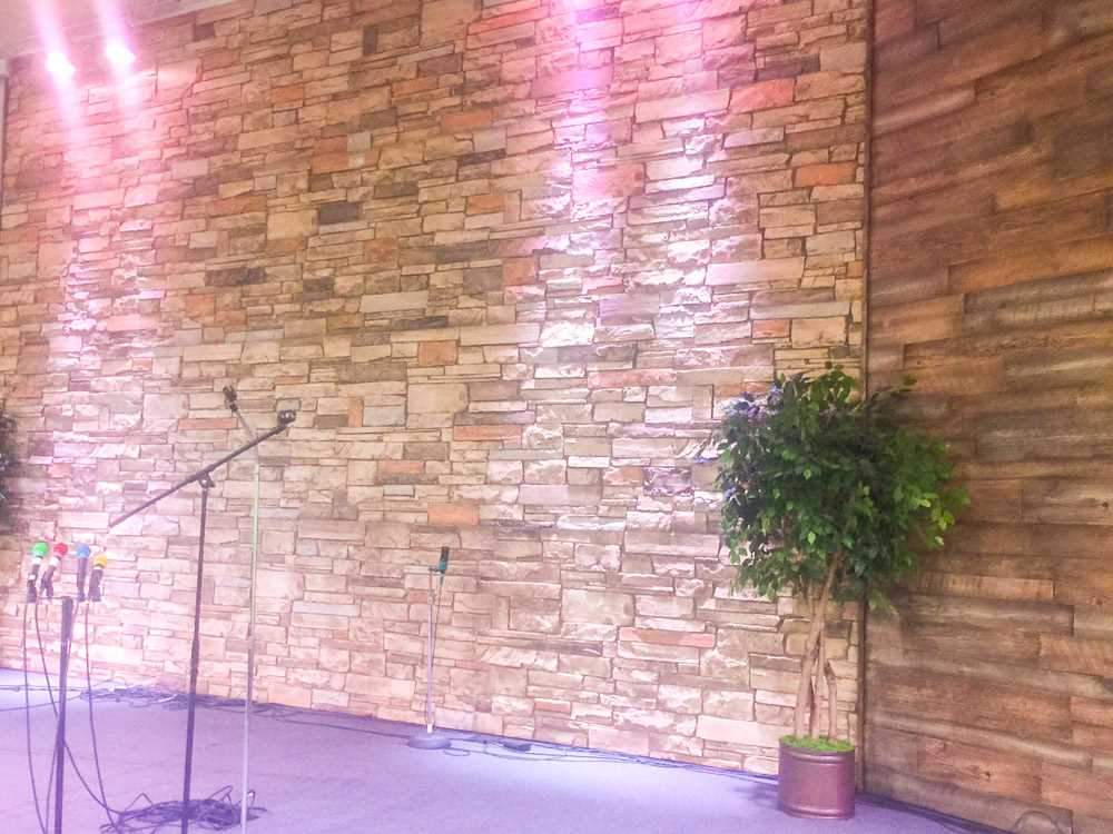 Interior stage wall mixing URESTONE faux stone panels with reclaimed faux wood accent; warm lighting.