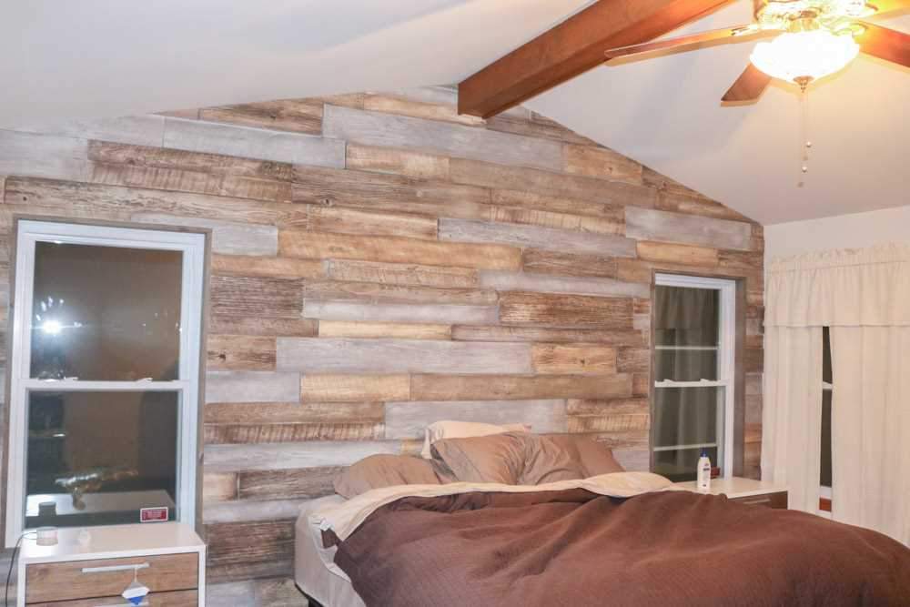 Primary bedroom feature wall in URESTONE reclaimed faux wood panels warm driftwood tones, staggered planks.