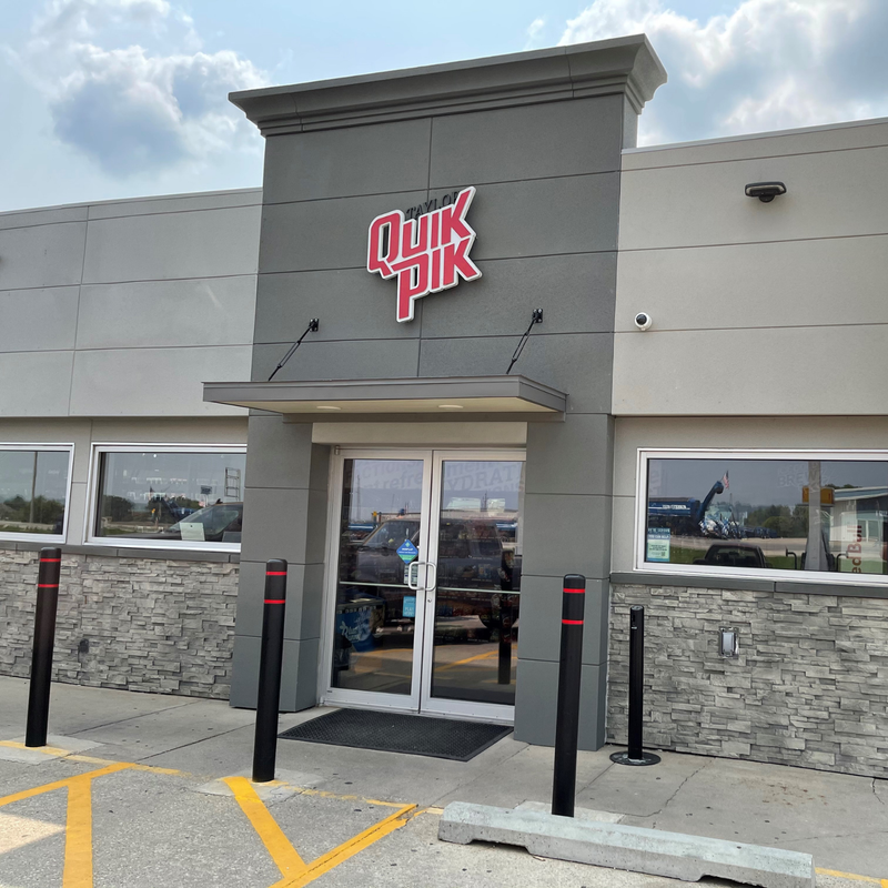 Quik Pik store front with logo featuring stacked stone wainscot and stucco in grey tones.