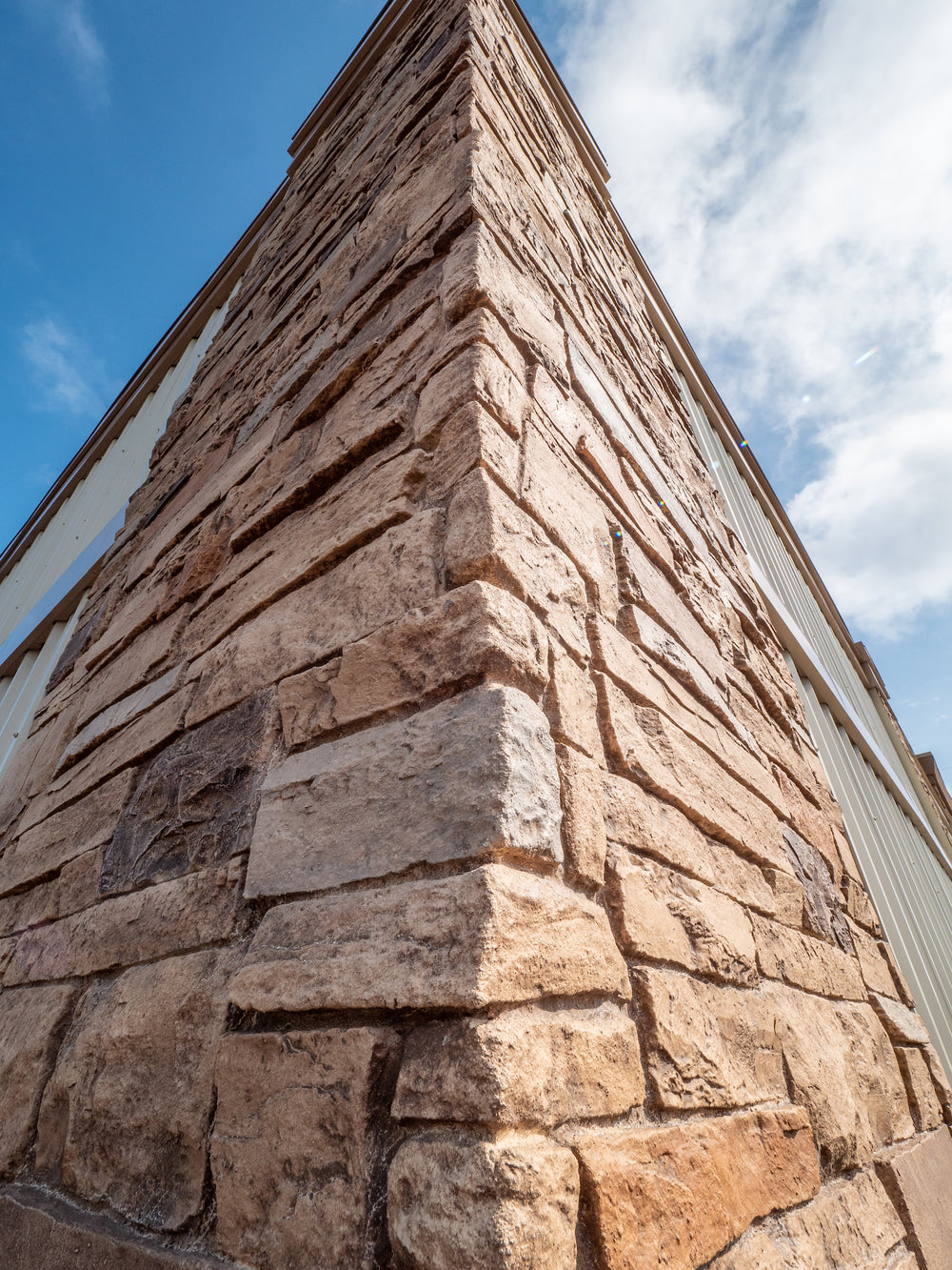 Close-up of a Ledgestone corner, hand-painted faux stone finish, hyper realistic stacked stone texture with a blue sky and clouds in the background