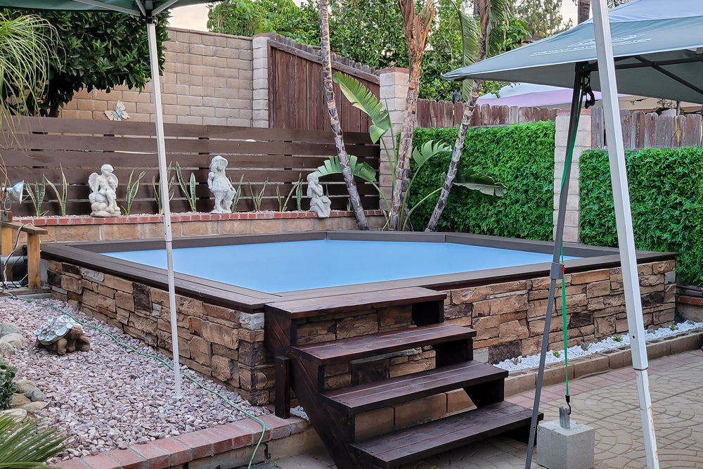 In-ground pool with hyper realistic stone coping and wooden steps in a backyard setting.
